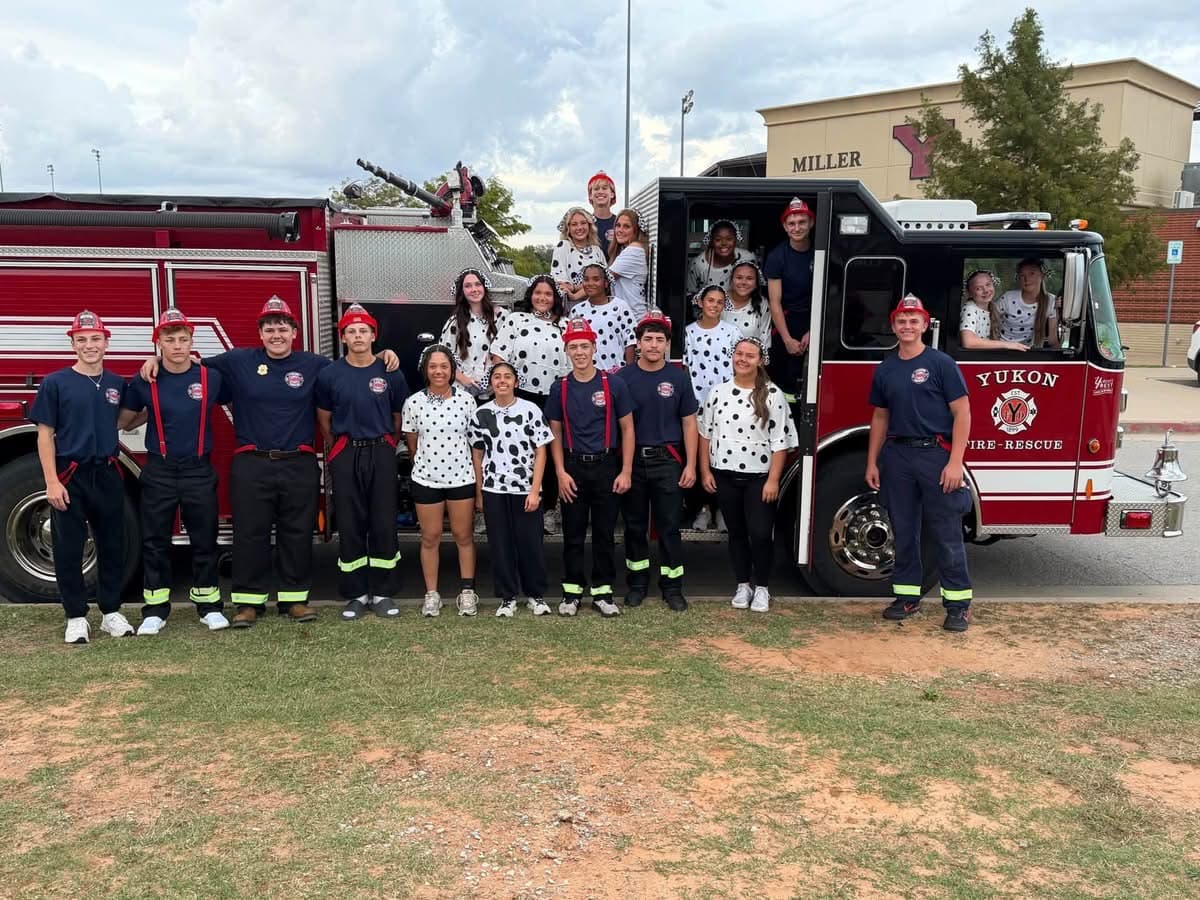 Powder Puff participants in firefighter uniforms and dalmatian-print shirts pose with a Yukon Fire-Rescue truck