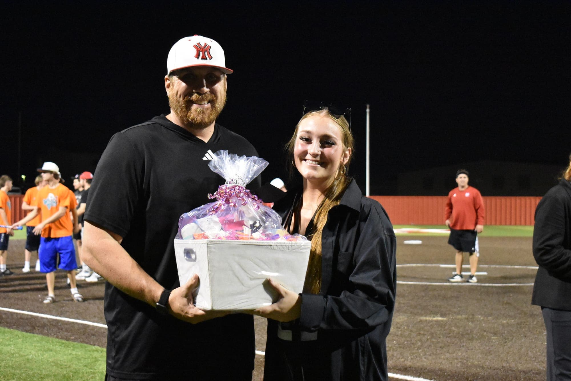 A Powder Puff participant and an adult hold a gift basket on the field