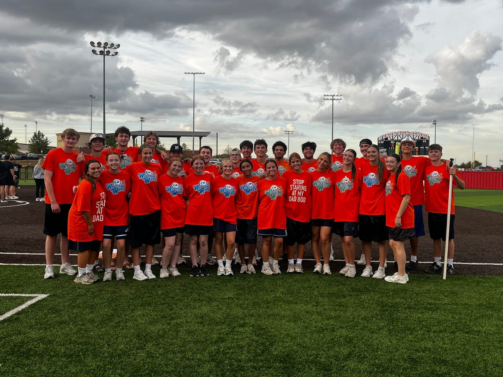 Powder Puff participants in matching orange shirts pose on the field at Yukon High School
