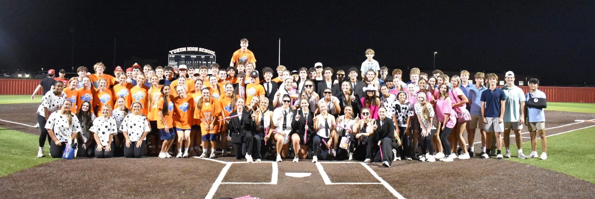Yukon Powder Puff 2026 participants gathered on the field at home plate in front of the Yukon High School scoreboard